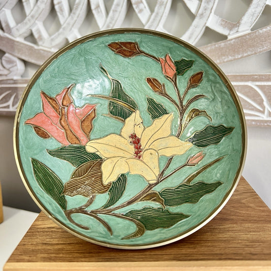 Decorative brass bowl with floral design on a wooden stand