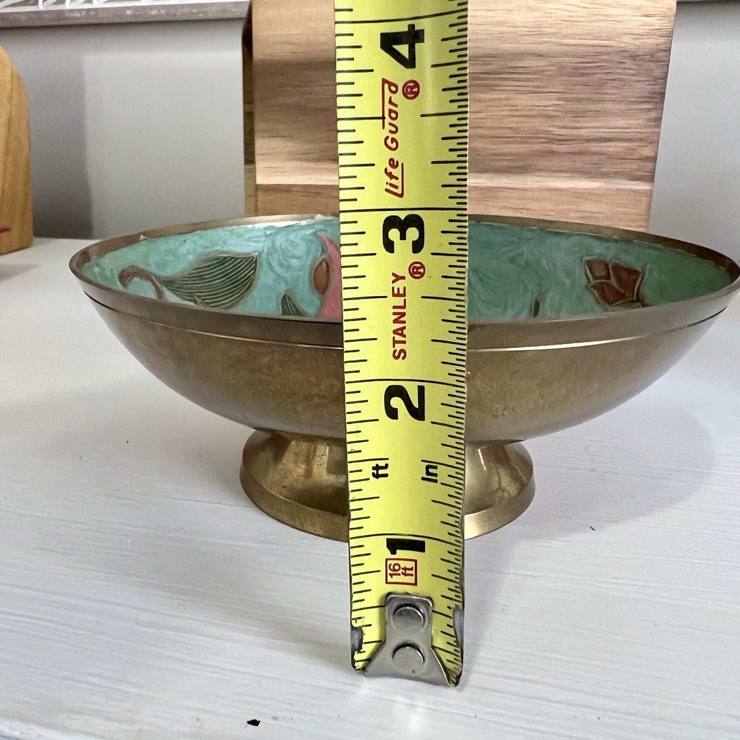 Brass bowl with decorative interior, placed on a white surface with a measuring tape for scale.