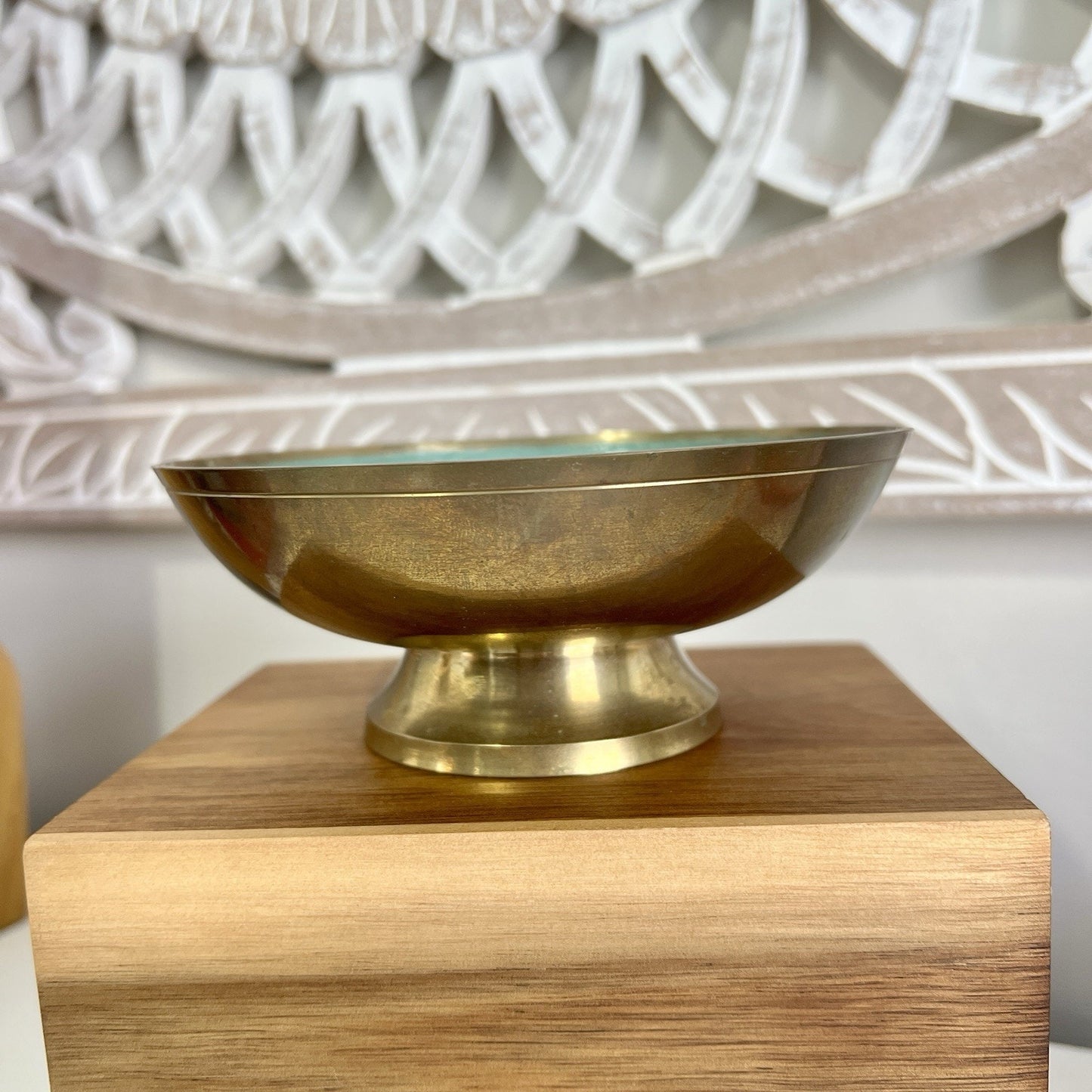 Brass bowl on a wooden pedestal with decorative wall in the background