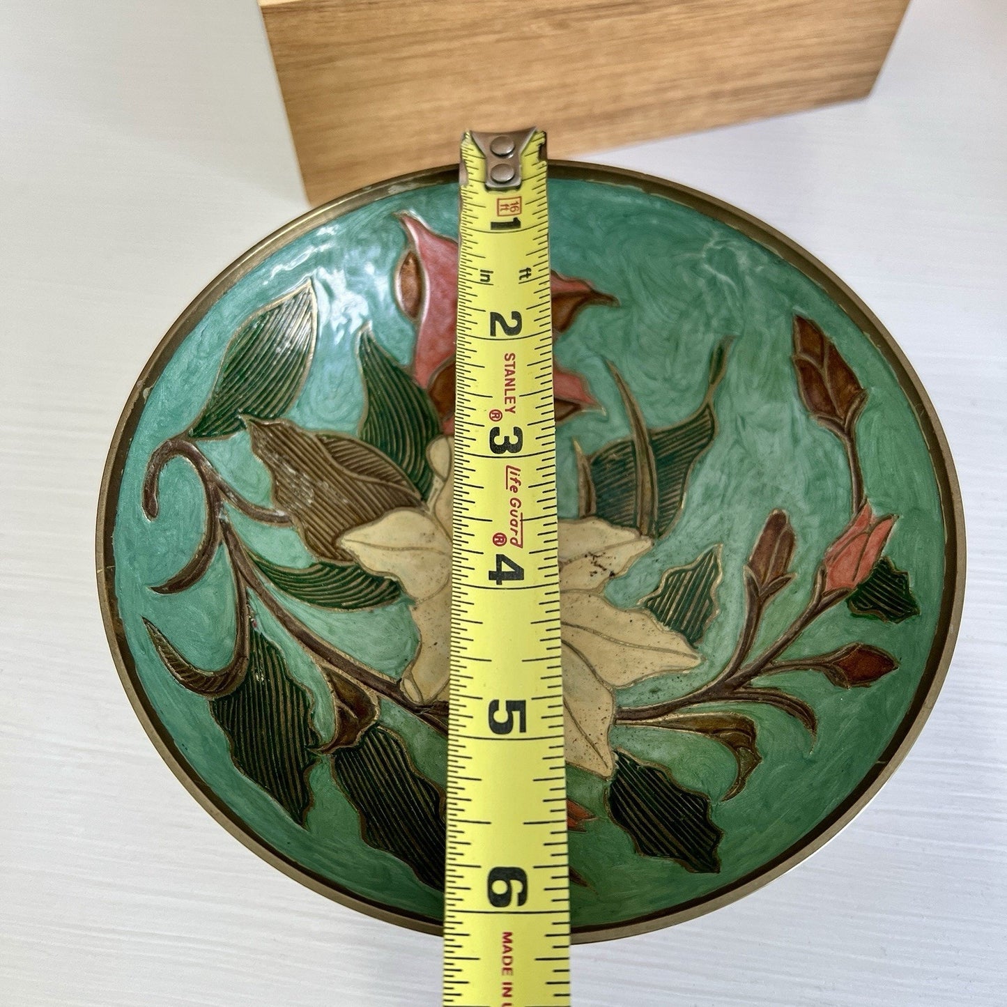 Decorative bowl with floral design and a measuring tape for scale on a white background