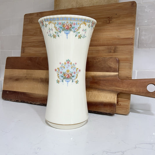 Decorative vase with floral patterns on a wooden cutting board against a tiled wall.