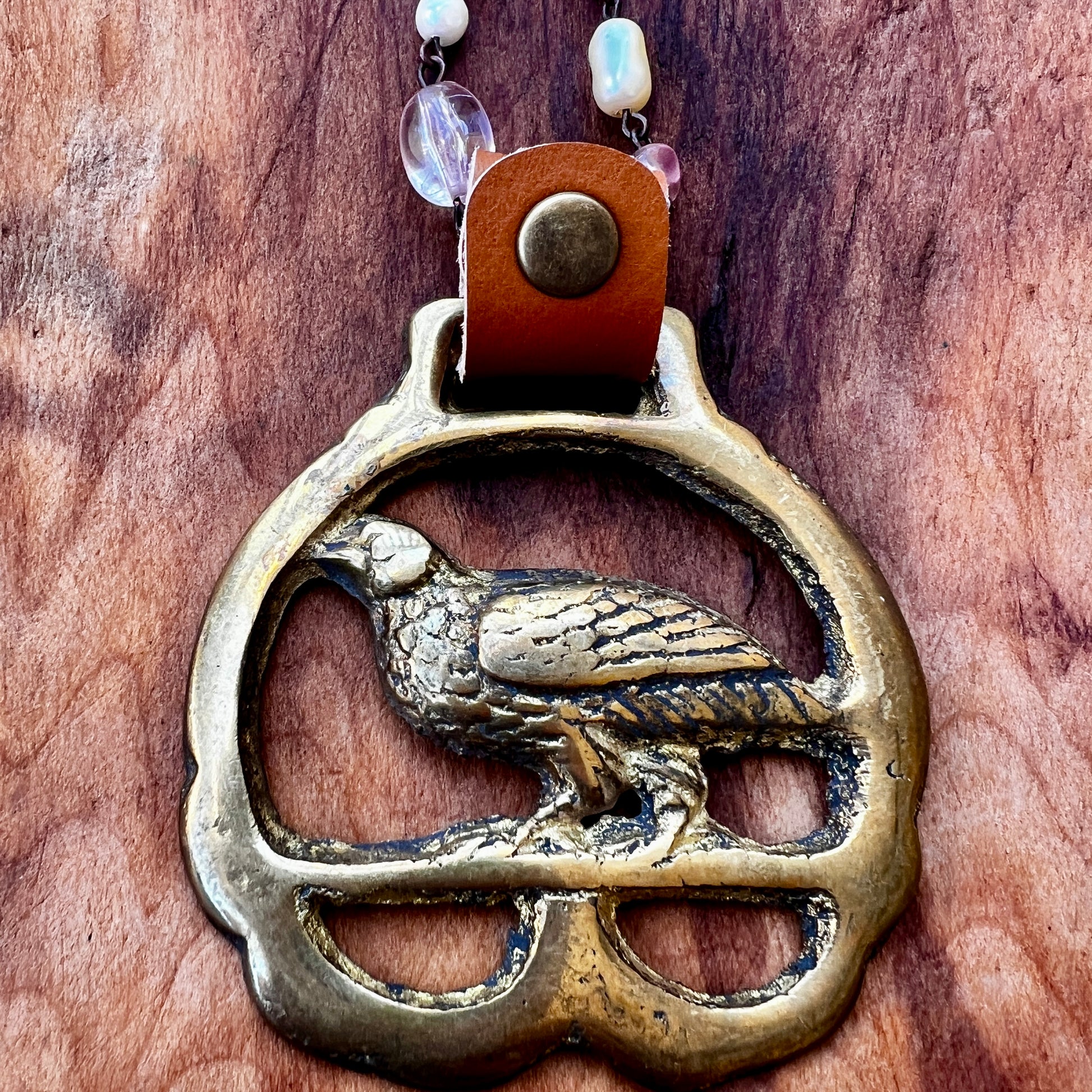 Brass bird pendant on a leather strap with beads against a wooden background