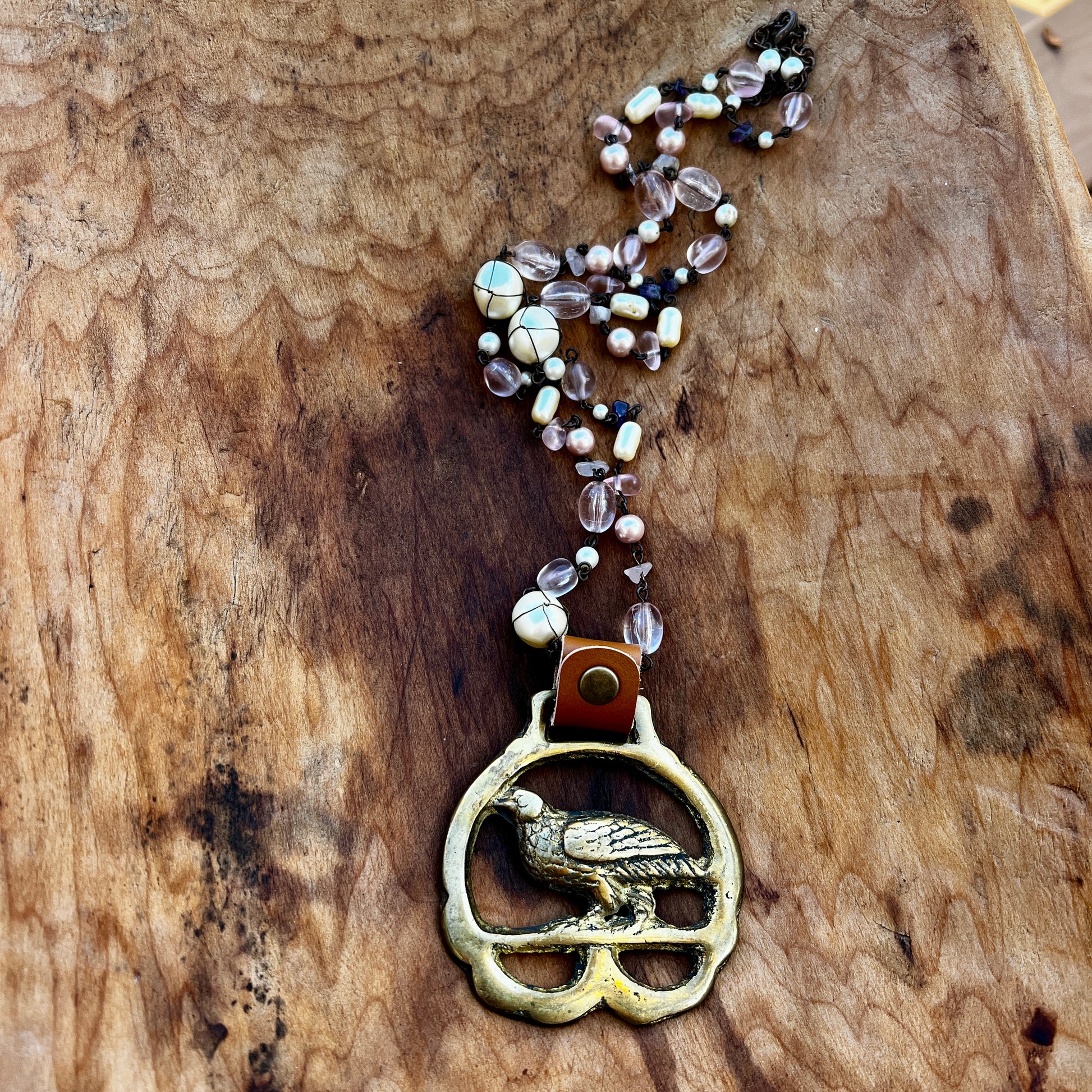 Necklace with a bird pendant and beaded chain on a wooden surface